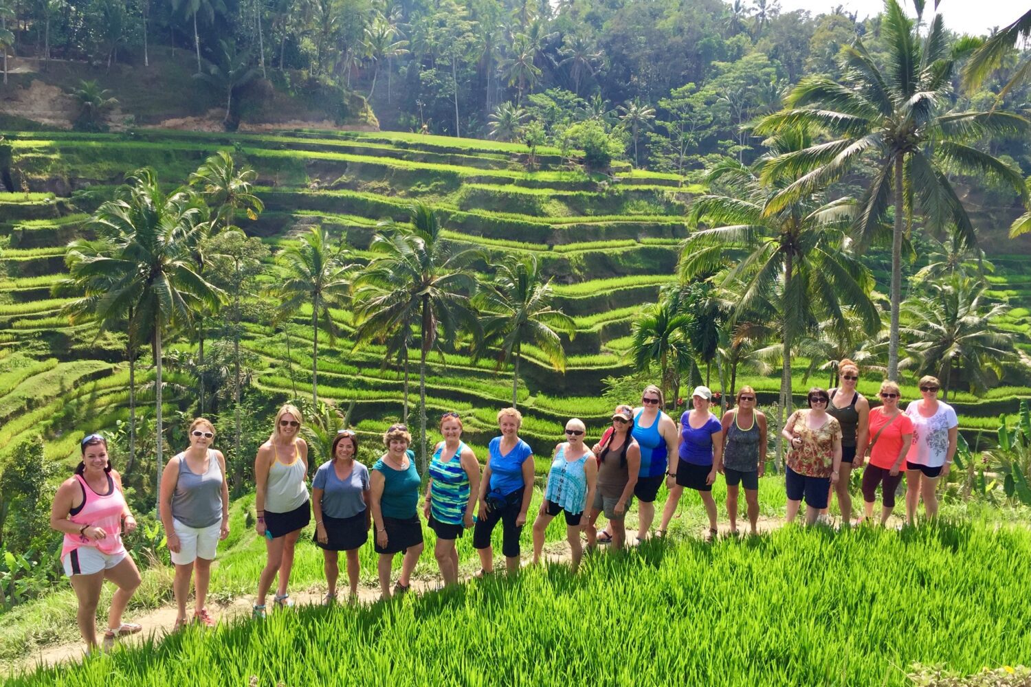 Group of smiling women standing in a line with Bali rice terraces behind them