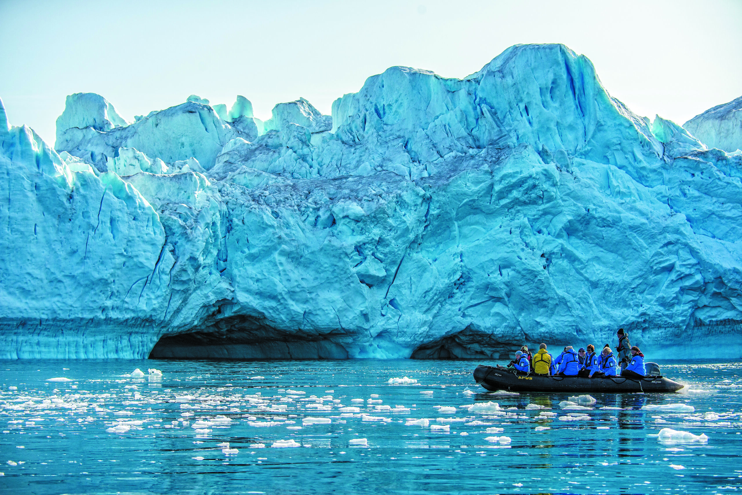 A group of people in a small inflatable boat exploring icy waters near a towering blue glacier in the Arctic - Out of the Northwest Passage