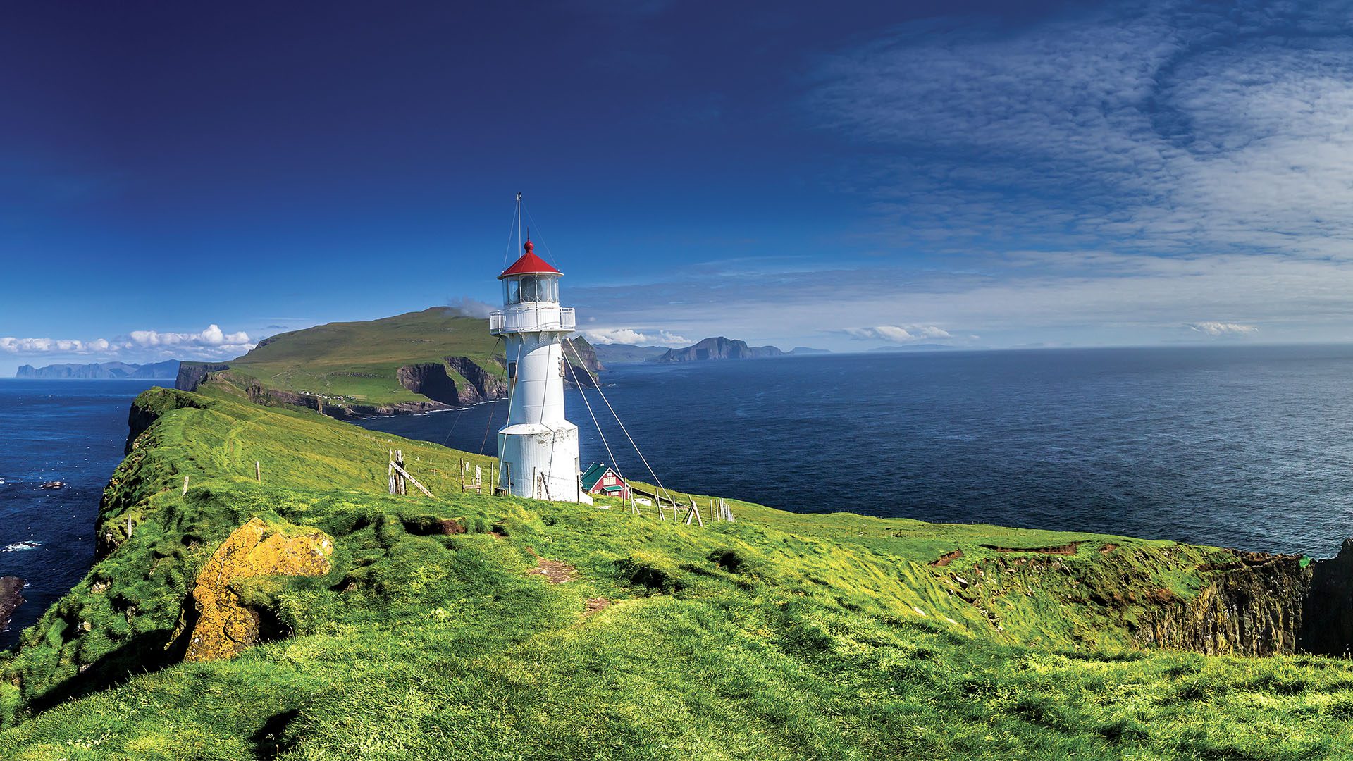 A picturesque white lighthouse with a red roof perched on a grassy cliff overlooking the vast blue ocean.