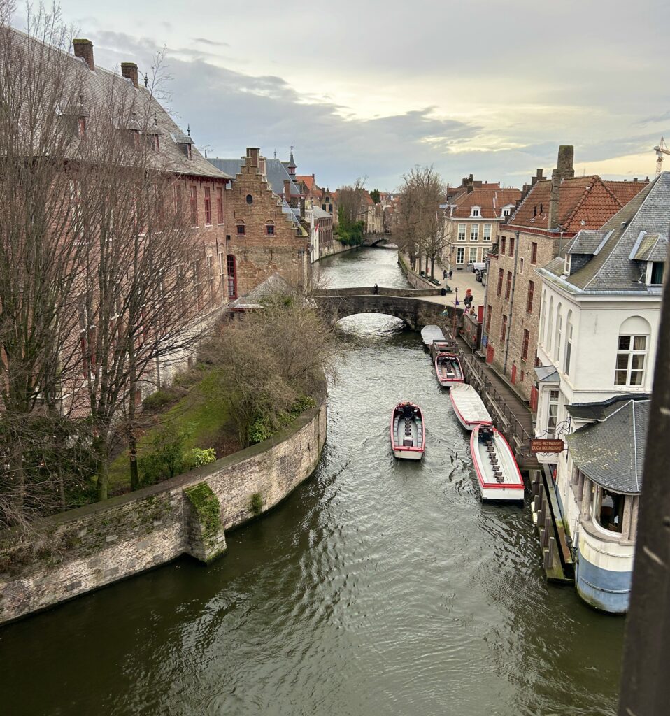 A boat floats down a canal on an overcast day in Bruges, Belgium to illustrate Hotel Bourgoensch Hof, a recommended accommodation on the Women's Travel Directory.