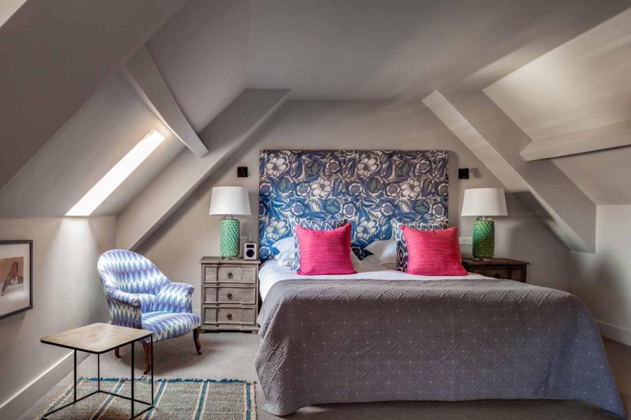 Interior of a junior king room at the Falstaff Hotel in Canterbury shows a stylish, simple room and a bed with a floral headboard and pink pillows.