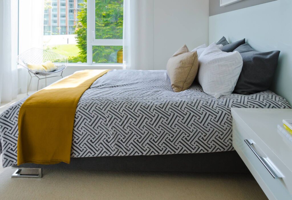 A simple bedroom with black and white cover and mustard yellow blanket at the food of the bed as an accent. Homestay.com