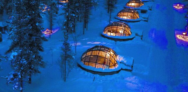 Glass-domed igloos glow warm against the snow at nightfall. The Northern Lights of Finland - Collette Travel