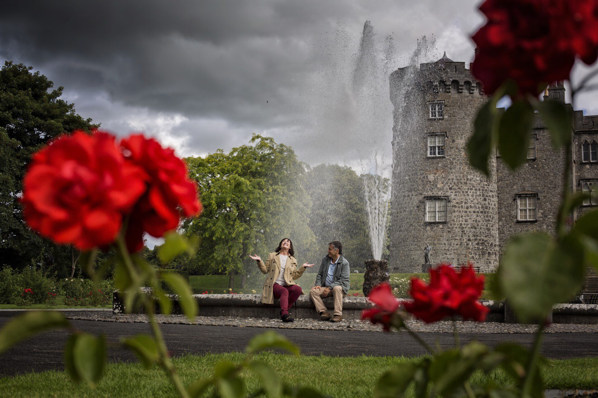 a couple sitting in the fountain laughing enjoying a cloudy afternoon at Kilkenny Castle - Irish Highlights - Brendan Vacations