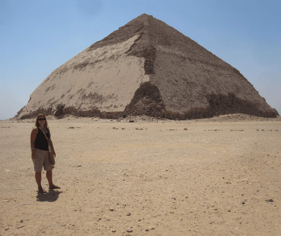 A woman stands in the desert in Egypt with a pyramid in the background. Invaders, Traders & Pyramid Builders - Inverted Atlas