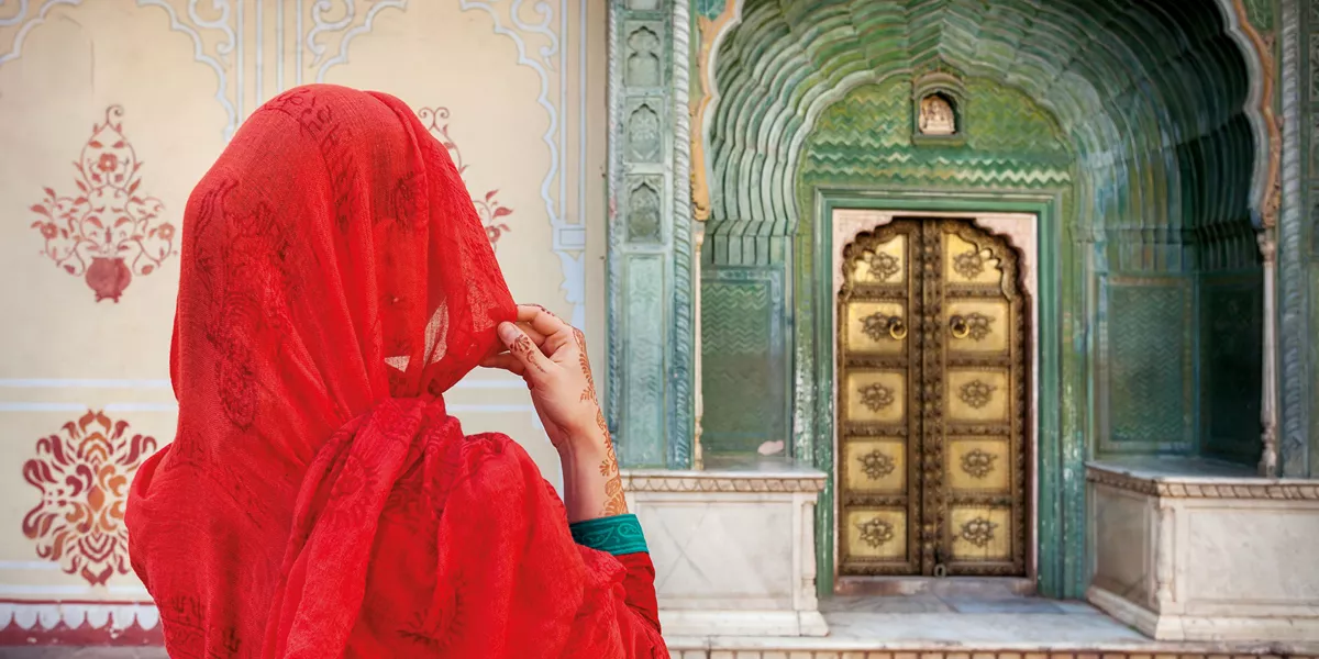 A woman wearing a vibrant red headscarf, striking a pose against the backdrop of intricately adorned Hindu architectural facade - CLASSICAL INDIA WITH NEPAL, A WOMEN-ONLY TOUR - Insight Vacations