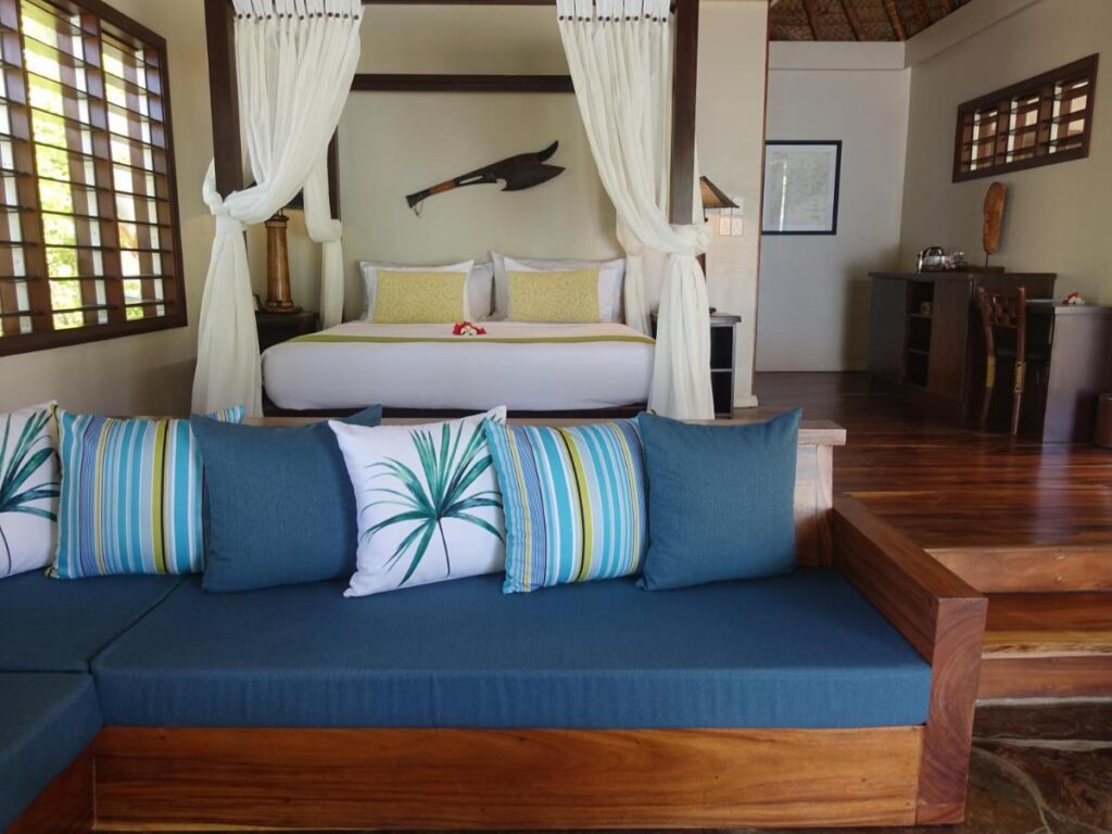A simple queen-sized bedroom with a bench at the Paradise Cove Resort in Fiji, recommended as a safe place for women to stay by a JourneyWoman reader.
