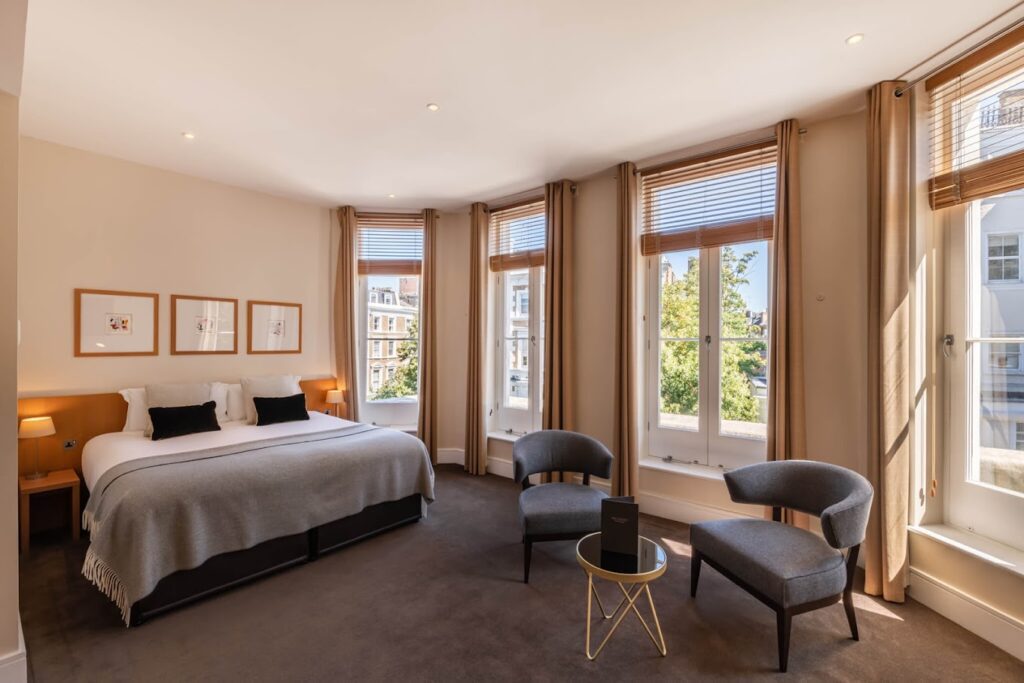 A suite with queen bed and multiple windows at the Nadler Kensington Hotel recommended as a safe place for women to stay by a JourneyWoman reader.