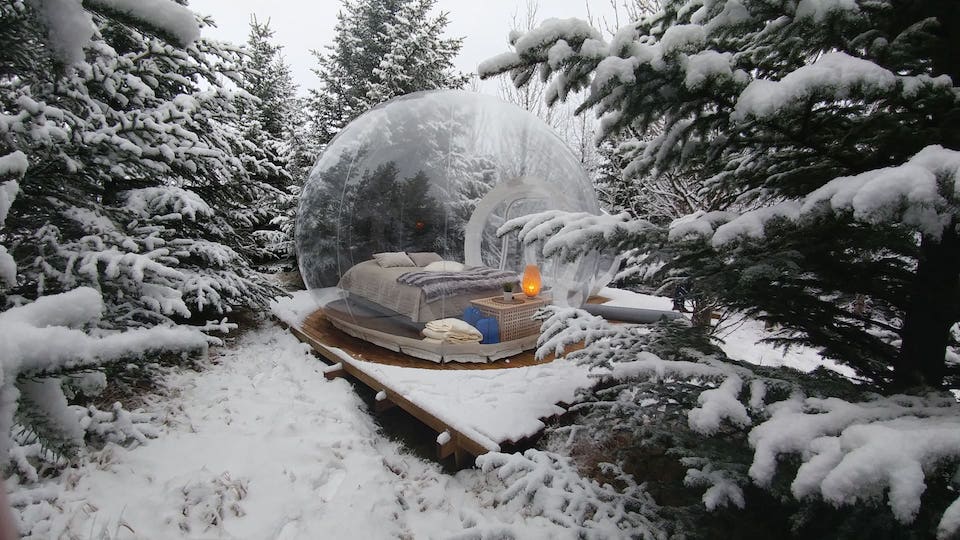 An exterior view of a Buubble hotel room, a clear dome containing a queen-sized bed in the snowy forest, recommended by a JourneyWoman reader as a safe place for women to stay.