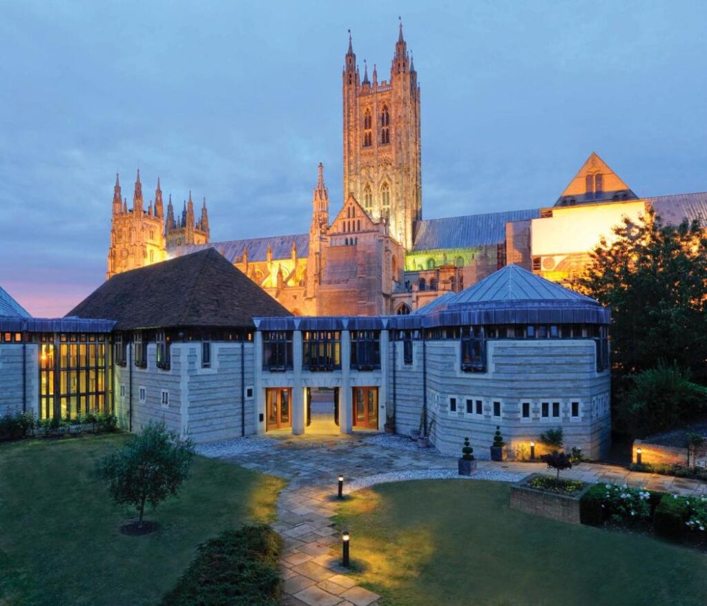 A view of the exterior of the Canterbury Cathedral Lodge in Canterbury, England, UK, at dusk—recommended by a JourneyWoman reader as a safe place for women to stay.