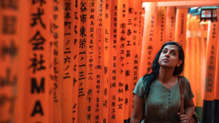 A woman walking through the vibrant orange torii gates of the Fushimi Inari Shrine in Kyoto, Japan