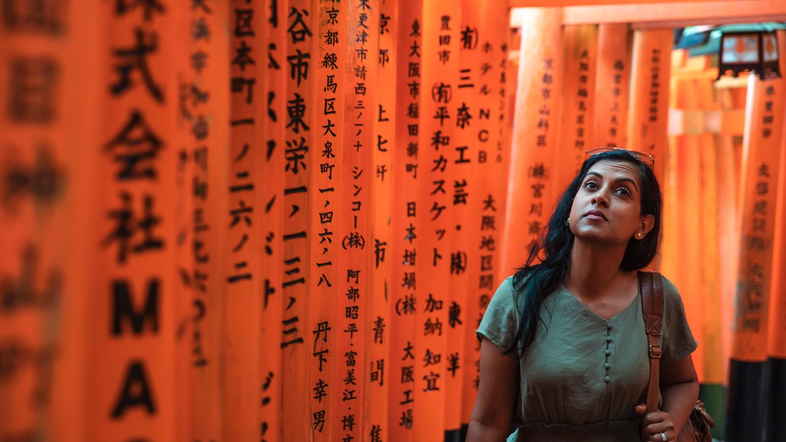 A woman walking through the vibrant orange torii gates of the Fushimi Inari Shrine in Kyoto, Japan