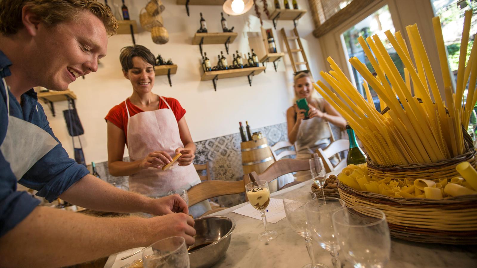 A group of travelers gathered, joyfully making pasta together in a lively, hands-on cooking experience.