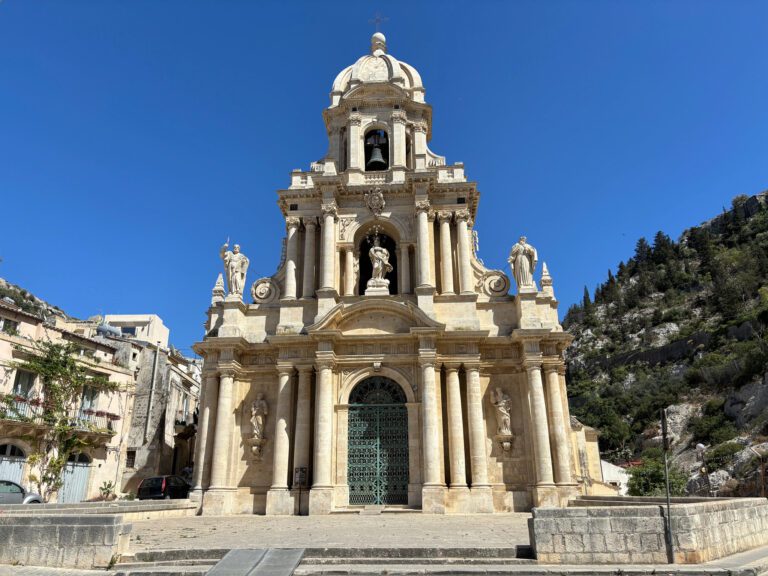 San Bartolomeo Church in Sicily, featuring its stunning Baroque architecture with intricate details, towering bell tower, and beautiful stone facade against a clear blue sky.