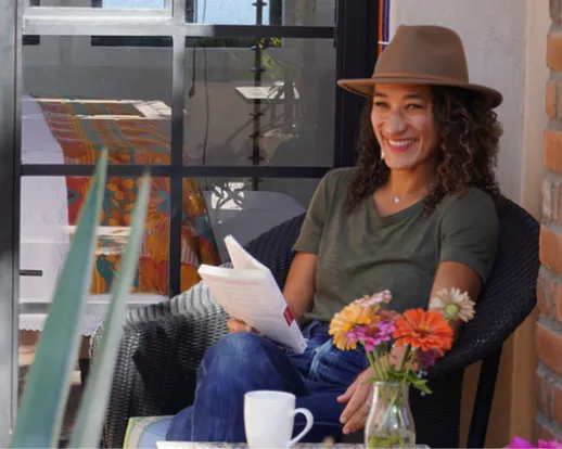A middle-aged woman in a hat sits at a chair with a notebook in her lap, part of a retreat led by Pico Iyer, with Modern Elder Academy.