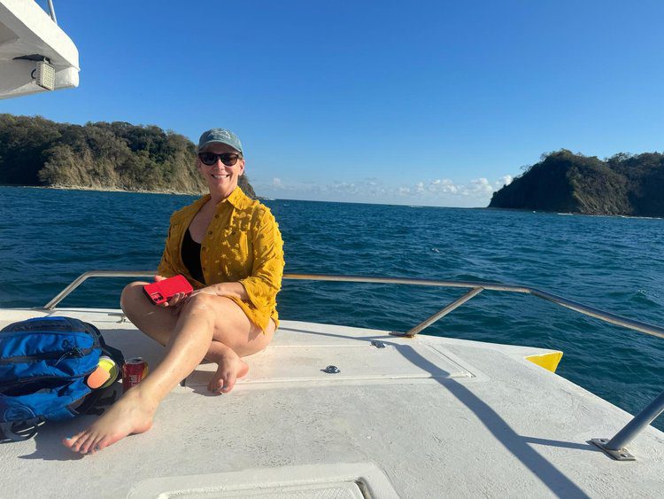 A smiling woman in a yellow top sits on a sailboat enjoying her Costa Rica Adventure with Bold Spirit Travel.