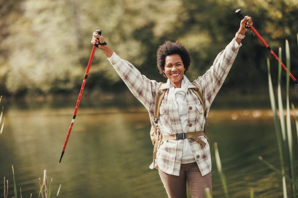 Older woman hiking on trail with arms raised holding hiking poles