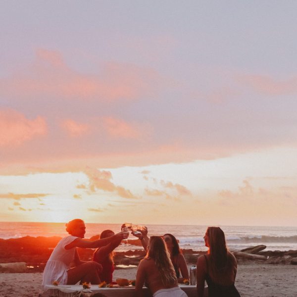 A group of women sit around a campfire on the beach at sunset - Sororal x Costa Rica