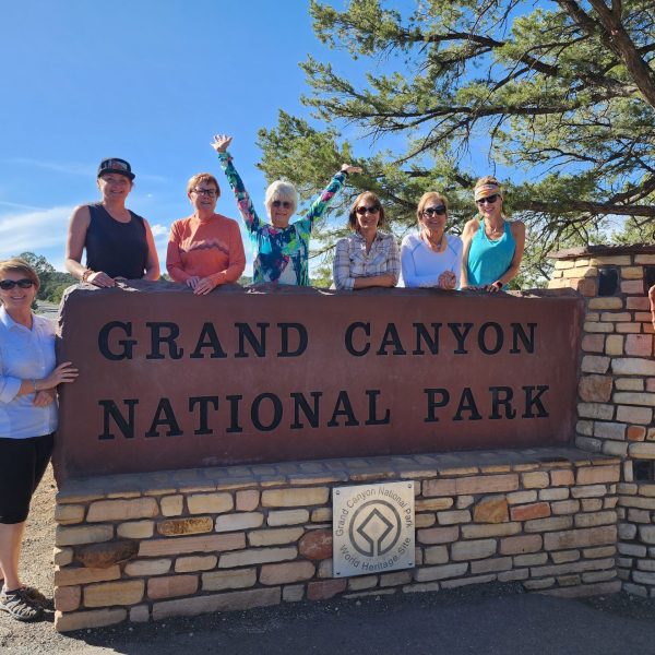 A group of women from the 'Canyons of the American Southwest' tour standing by the Grand Canyon National Park sign.