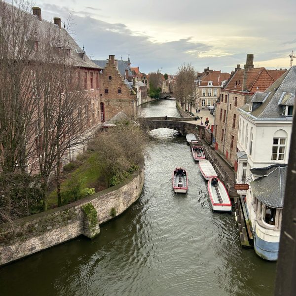 A boat floats down a canal on an overcast day in Bruges, Belgium to illustrate Hotel Bourgoensch Hof, a recommended accommodation on the Women's Travel Directory.