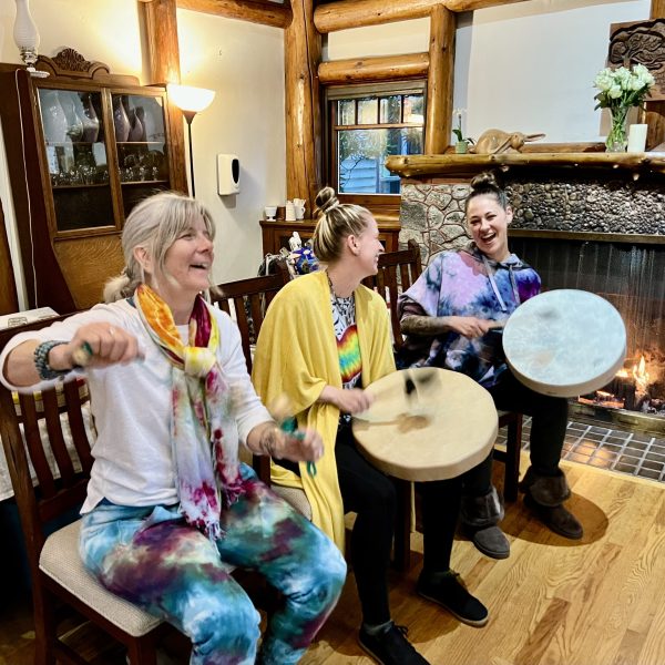 Three women in brightly coloured clothing lead a drum circle as part of the Between the Solstice & the Strawberry Moon Yoga Retreat hosted by Jeni's Global Yoga Trips