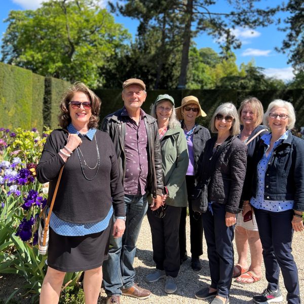 A small group of happy travelers - six women and one man - stand in a garden in Paris. Inside Paris - European Experiences