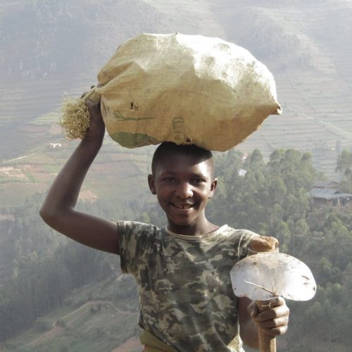 Smiling young Ugandan woman balancing sack on her head - Women Tour Uganda