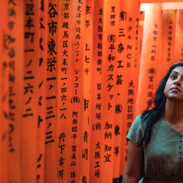 A woman walking through the vibrant orange torii gates of the Fushimi Inari Shrine in Kyoto, Japan