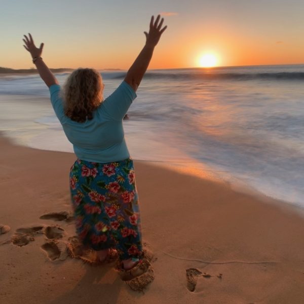 Women savoring a serene moment on the beach as the sun sets, casting warm hues across the sky and ocean.