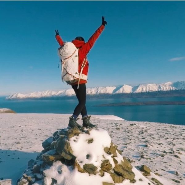 A women standing on a snowy hill with arms raised, overlooking a fjord in North Iceland.-North Iceland Yoga Adventure