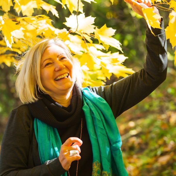 A woman admiring the vibrant colors of the trees and dappled sunlight in the woods.