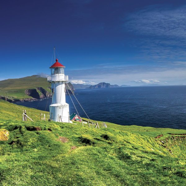 A picturesque white lighthouse with a red roof perched on a grassy cliff overlooking the vast blue ocean.