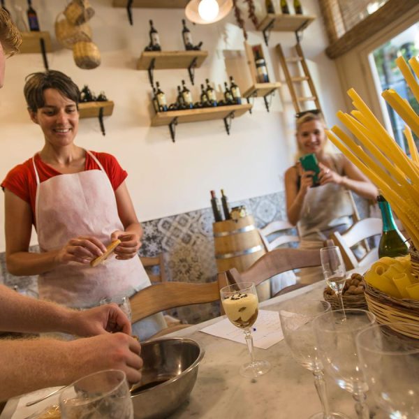 A group of travelers gathered, joyfully making pasta together in a lively, hands-on cooking experience.