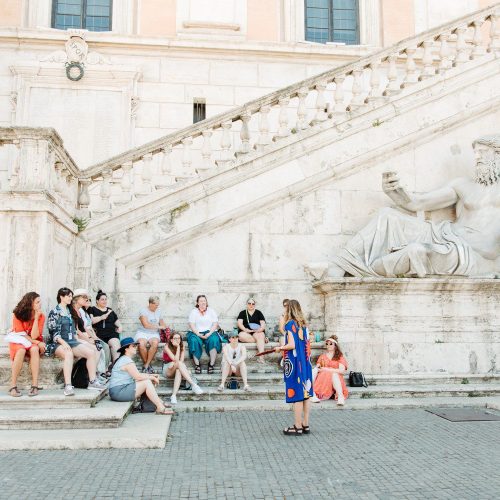 A group of women travelers sit on the steps of a historical site in Italy. Stellavision Travel