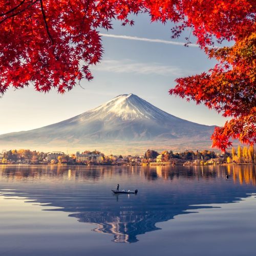 A view of Japan's Mount Fuji framed by red-tinted leaves and a mirror-calm lake. Collette Travel