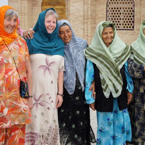 Two ElderTreks guests wearing headdress pose with local women as the group tours Central Asia.