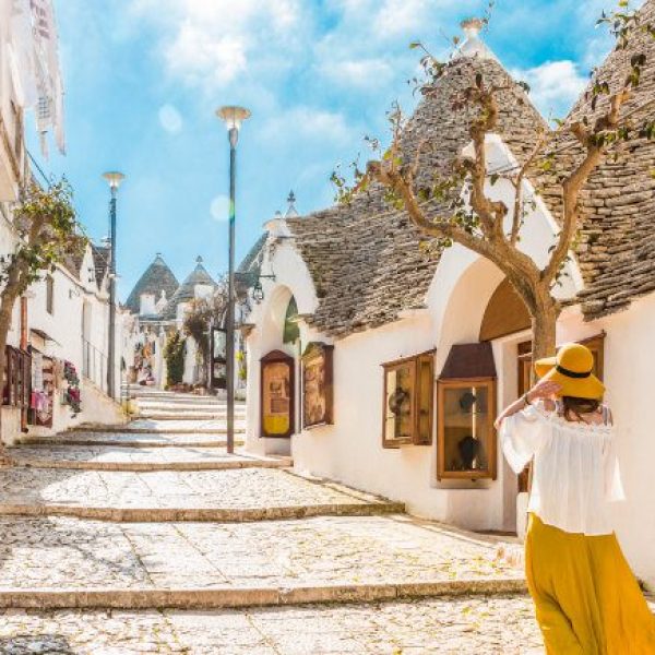 A woman in a flowing yellow skirt and had walks alone on a street in Fasano, a stop on the Discover Puglia tour by Just You.