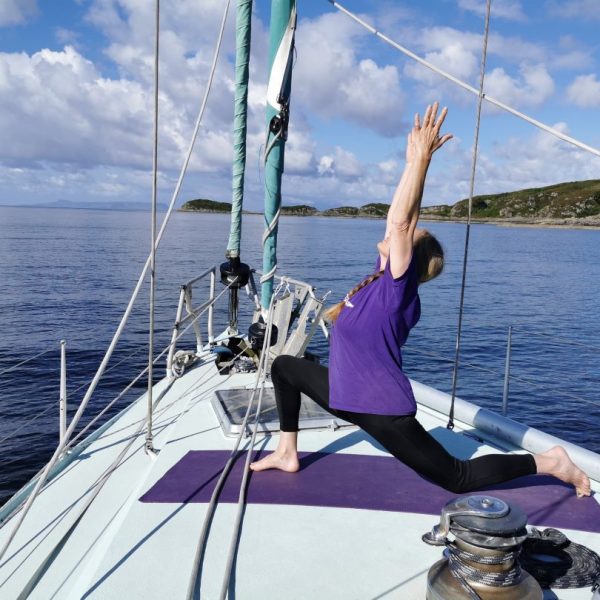 A woman practicing yoga both on the deck of the Selkie yacht and onshore, surrounded by serene nature - Mindful Sail and Wild Yoga Retreat