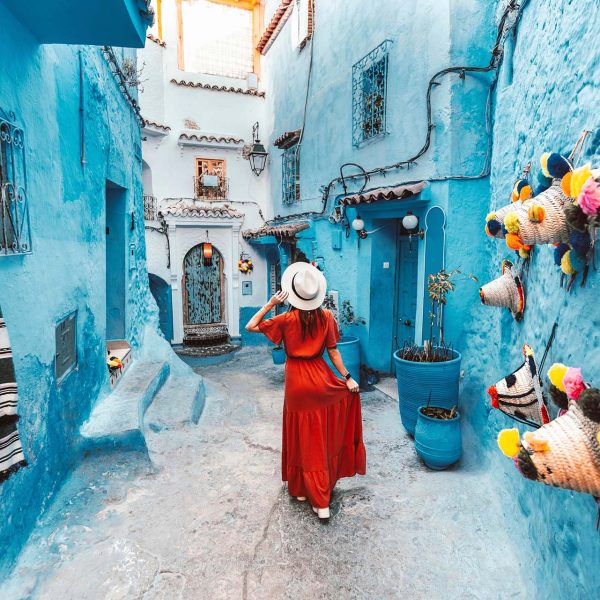 A woman in a vibrant red dress strolls through the picturesque streets of Chefchaouen - Wonders of Morocco - Sisterhood Travels