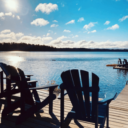 Muskoka chairs on the dock by the lake in Torrence, Ontario, part of the Muskoka Beer Spa, a JourneyWoman recommended safe place for women to stay.