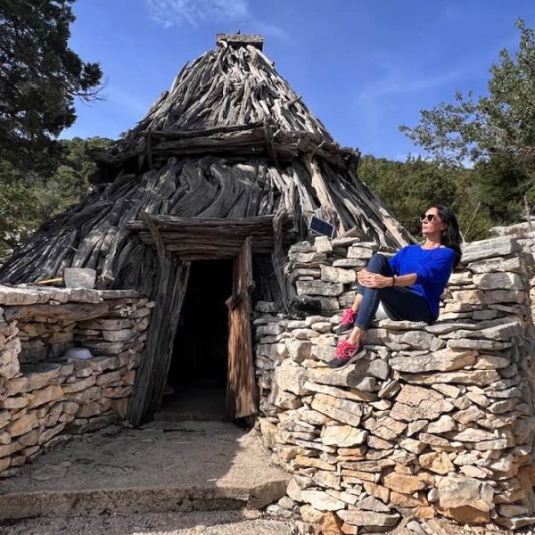 Angela Macaluso, founder of Sicily and Italy by Experts, sits on a hand-built stone wall outside a historical structure on the Women's Escape to Sardinia's Hidden Secrets tour.
