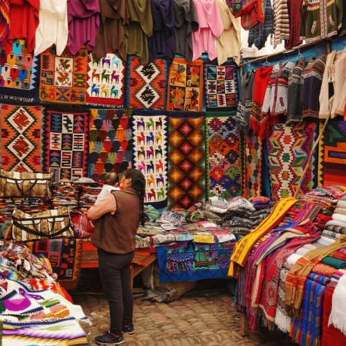A woman holding a baby stands inside a market stall with the walls and tables covered in indigenous tapestry—Centre for Good Travel