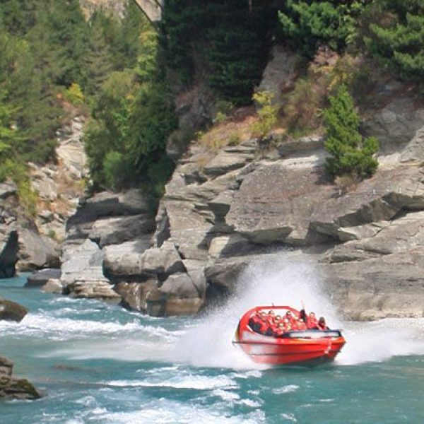 A boat speeds along a glacier river, a part of the Breathtaking New Zealand tour by Just You.