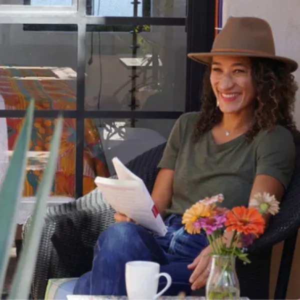 A middle-aged woman in a hat sits at a chair with a notebook in her lap, part of a retreat led by Pico Iyer, with Modern Elder Academy.
