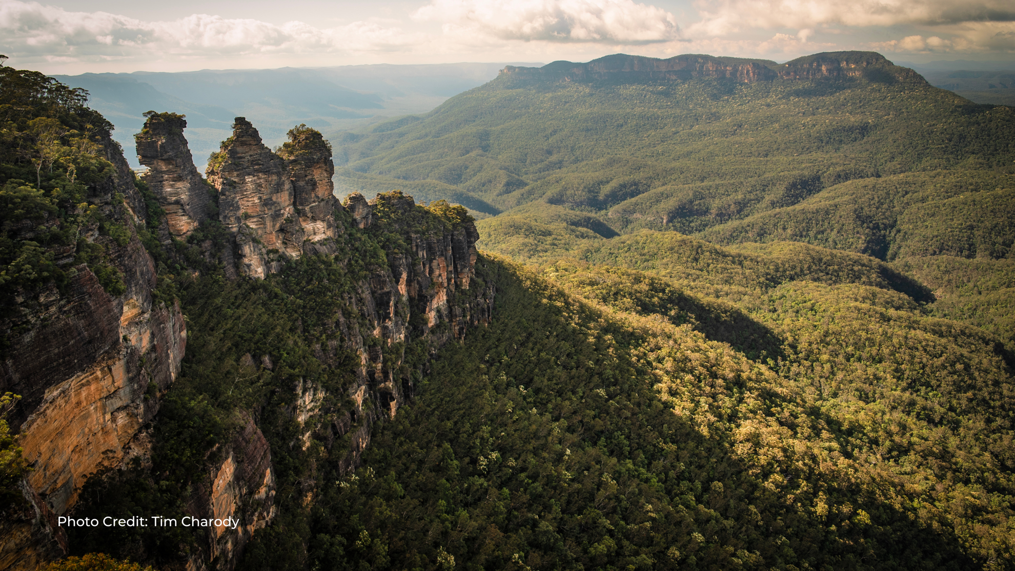 A breathtaking view of the Three Sisters rock formation overlooking a vast, forested valley in Australia’s Blue Mountains National Park.