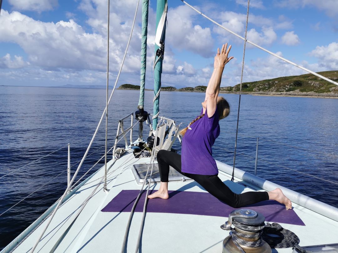 A woman practicing yoga both on the deck of the Selkie yacht and onshore, surrounded by serene nature - Mindful Sail and Wild Yoga Retreat