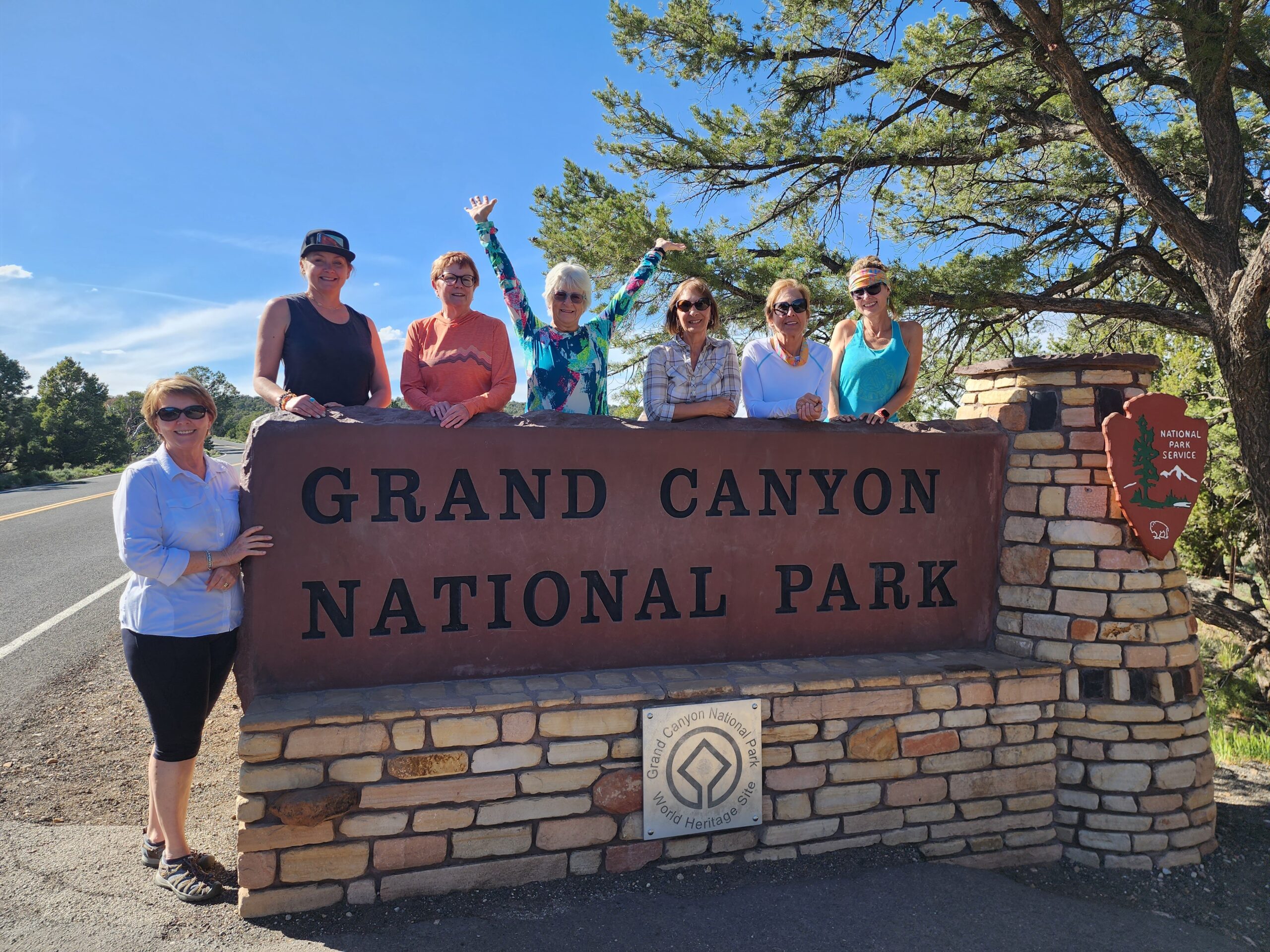 A group of women from the 'Canyons of the American Southwest' tour standing by the Grand Canyon National Park sign.