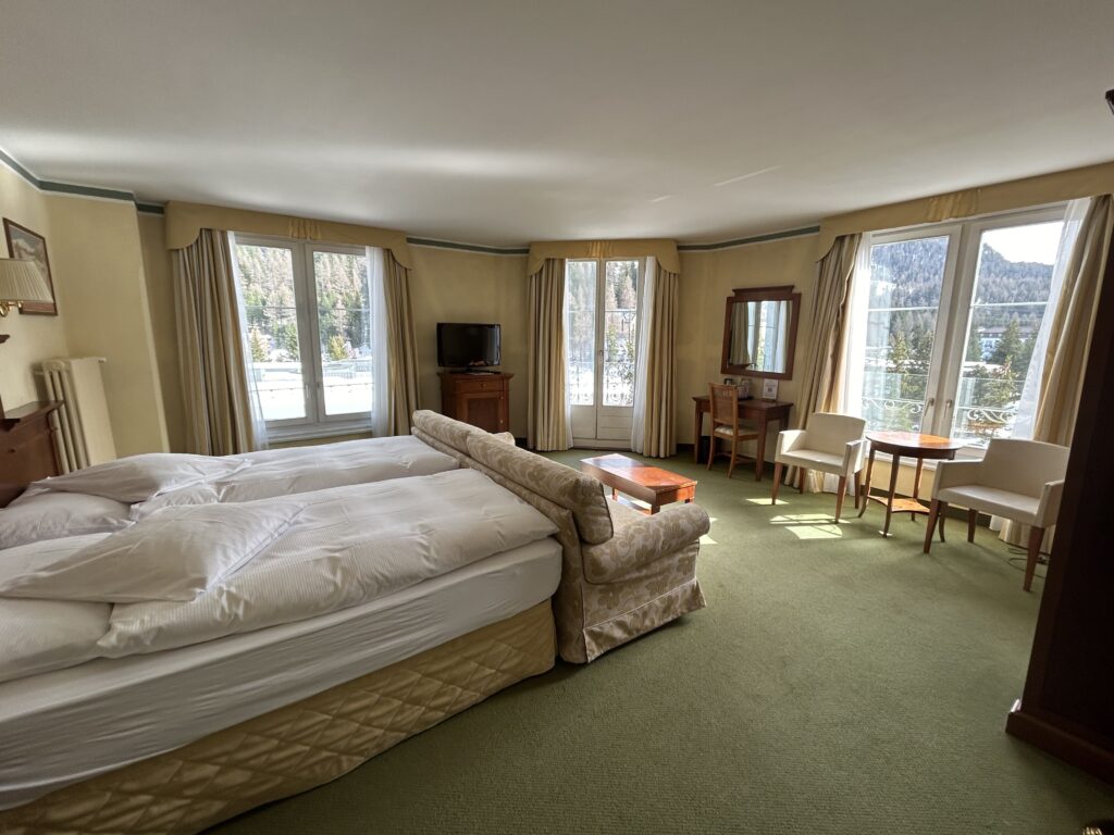A well lit room with comfortable bed and multiple windows at the Hotel Reine Victoria St. Moritz, Switzerland, recommended as a safe place for women to stay.