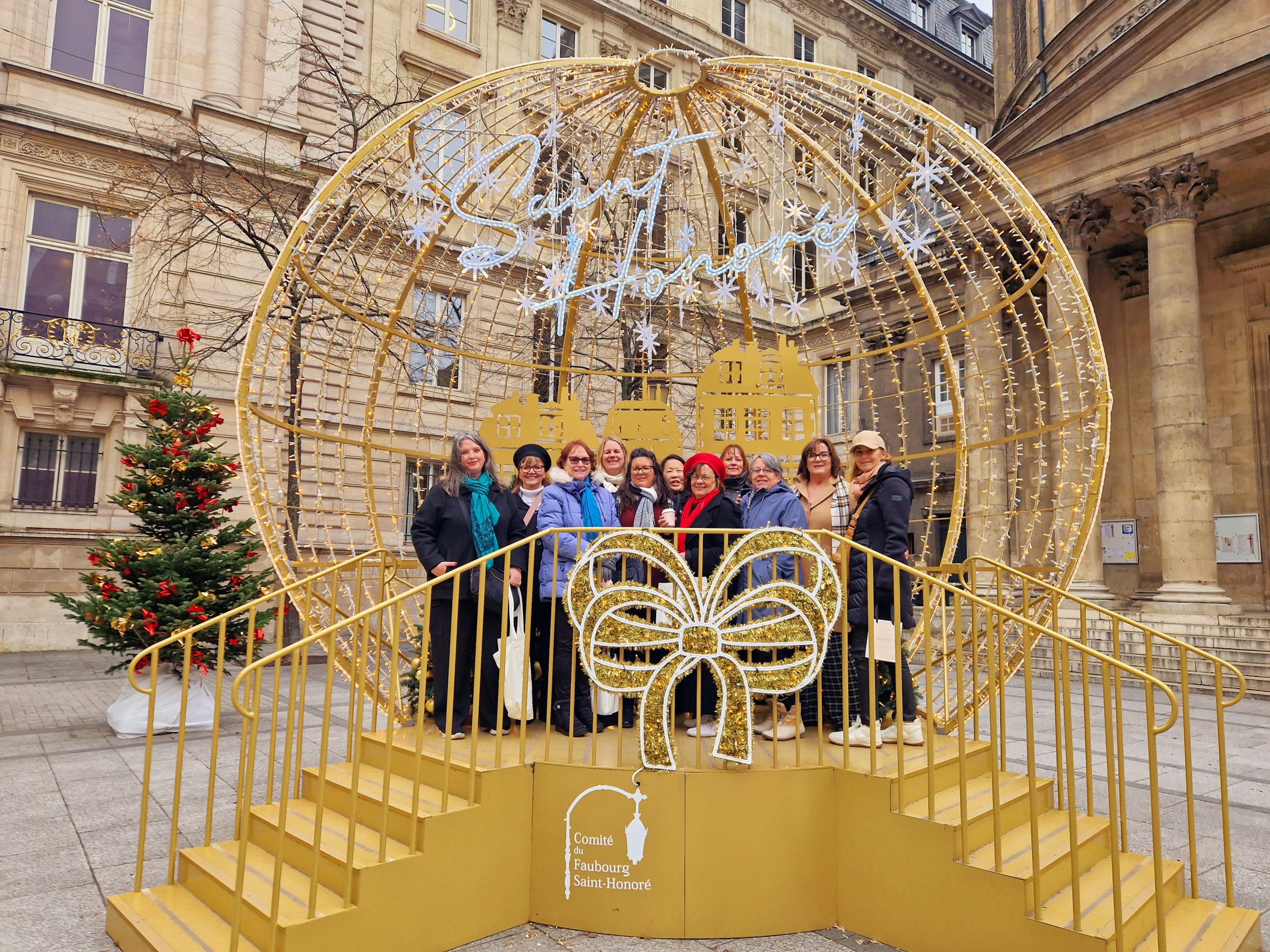 Guests of A Magical Christmas in Paris with bestselling author Steena Holmes posing under festive Christmas decorations.