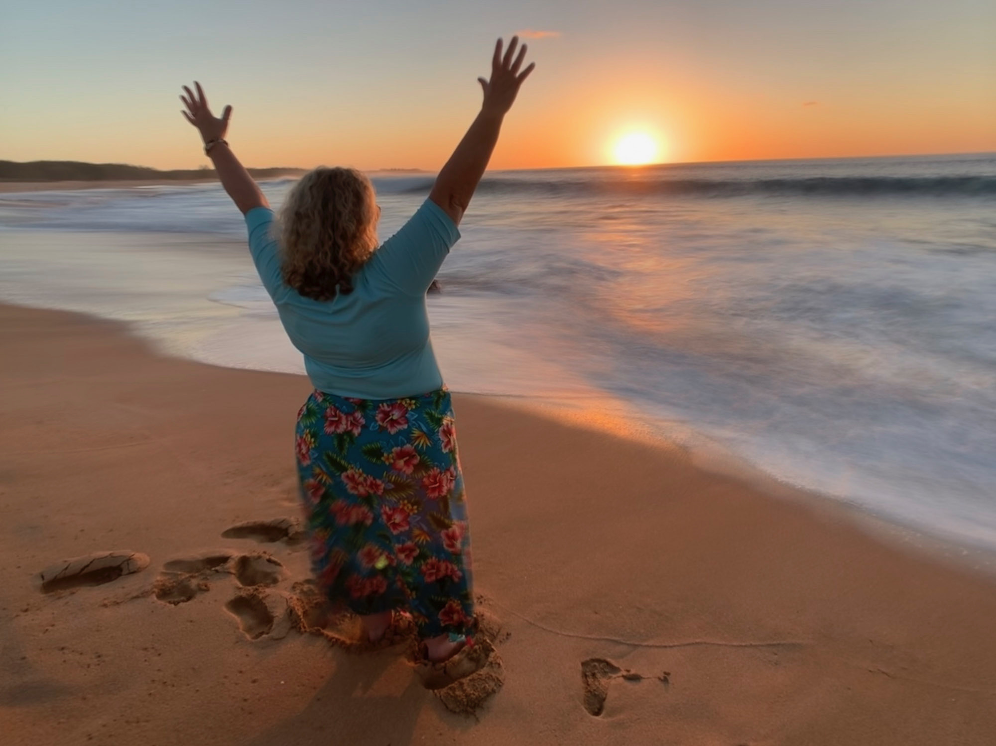 Women savoring a serene moment on the beach as the sun sets, casting warm hues across the sky and ocean.